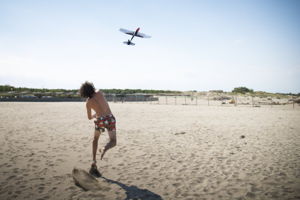 一个人把滑翔机或玩具飞机扔到海滩上。图片下载