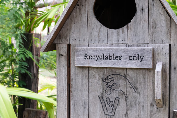 木质垃圾桶，上面有标识和标志，这个垃圾桶只用于可回收垃圾。自然和绿树在背景中模糊不清。环境保护，垃圾再利用和再循环理念。图片下载