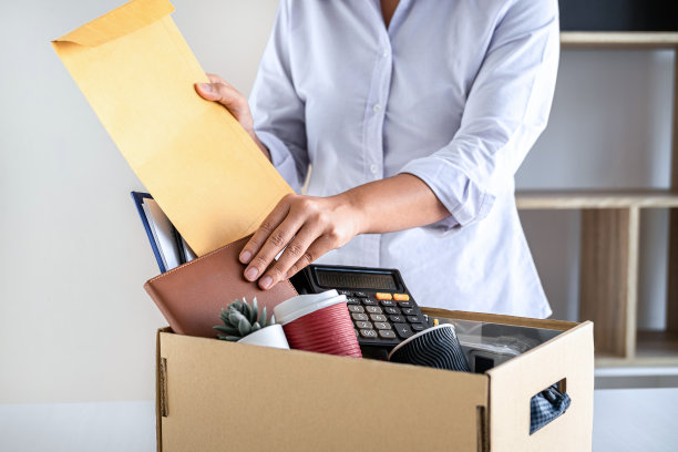 图片上的女商人正把他所有的私人物品和文件打包到一个棕色的纸板箱里，这让他感到沮丧和压力，不得不辞职并签署取消合同的信图片下载