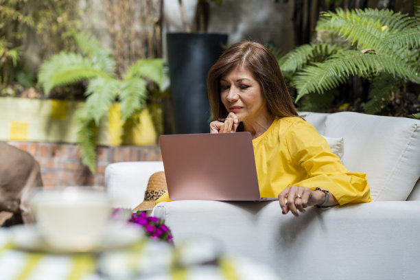 一位成年女性在自家花园里工作，穿着正装查看笔记本电脑图片下载