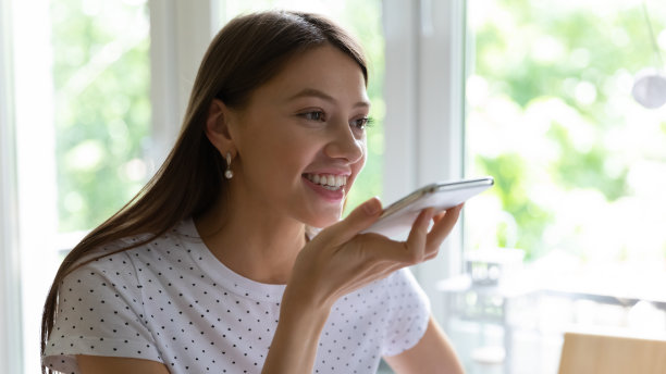 微笑的年轻女子使用手机上的数字语音助手图片下载