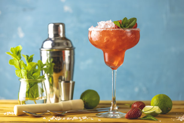 冰冻草莓酸橙薄荷玛格丽塔在高脚玻璃杯靠近与酒吧工具和配料的木桌。高档酒精鲜饮。图片下载