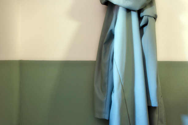 一间现代化的门厅里，半白半绿的墙上挂着一件绿色复古雨衣。现代风格图片下载