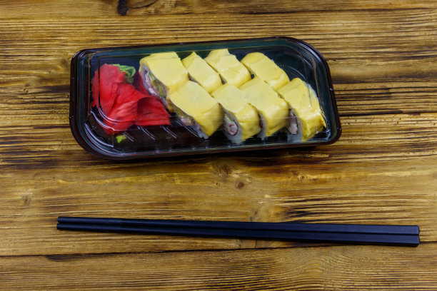 寿司芝士卷在塑料盒里放在木桌上。装在塑料容器内的寿司供外卖或运送图片下载