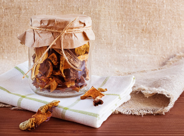 干蘑菇装在一个玻璃罐里，上面盖着纸，放在一张木桌上。粗麻布的背景。有机、环保食品图片下载