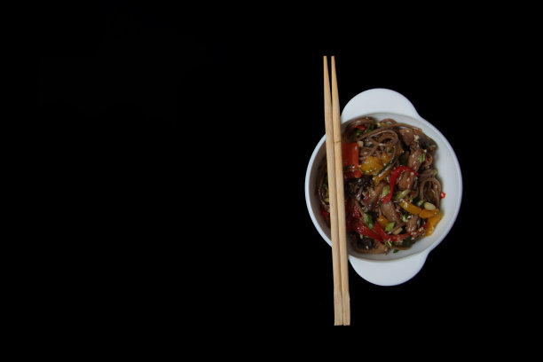 一碗炒面和筷子孤立在黑色的背景上平躺着图片下载