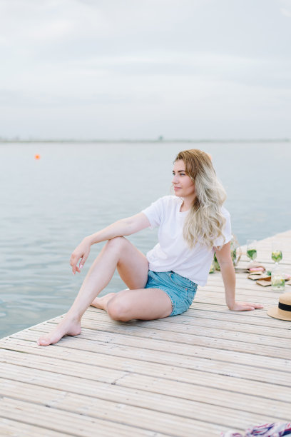 一个穿着白色t恤的女人坐在水边的木制码头上。布隆代,微笑图片下载