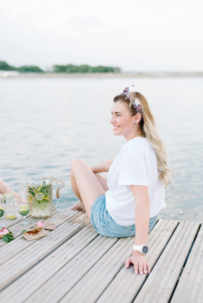 一个穿着白色t恤的女人坐在水边的木制码头上。布隆代,微笑图片下载