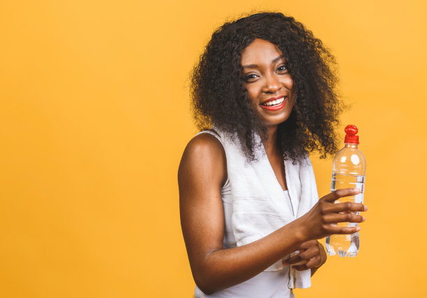 美丽迷人的年轻出汗的非洲裔美国黑人妇女饮水锻炼后，补水解渴，孤立在黄色背景。图片下载