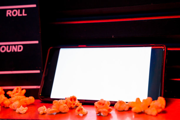 手机与空白色明亮的屏幕爆米花桶和电影拍板。在互联网手机上播放电视的概念。图片下载