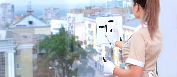 Robot-window-cleaner。在酒店或家里打扫卫生。一个穿制服的女孩在机器人的帮助下清洗窗户。漫长的旗帜。认不出来照片。图片下载