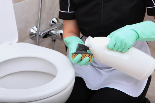 女人们戴着绿色橡胶手套的手把洗涤剂倒在海绵上。在浴室里打扫厕所。认不出来照片。清洁和卫生的概念。图片下载