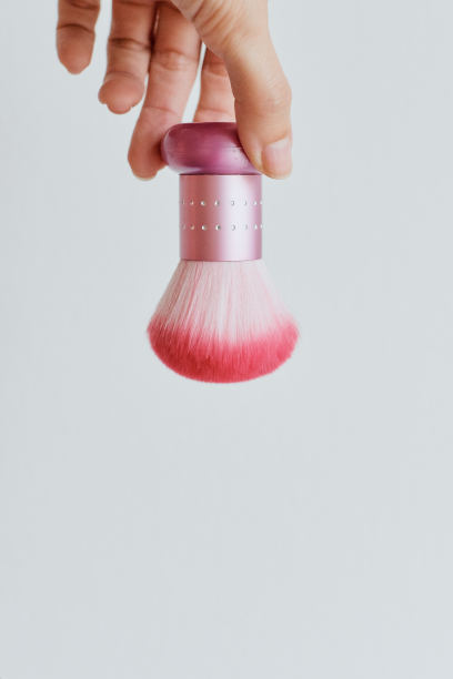粉色刷子用于清除指甲上的灰尘或粉末。一把镶着水钻的刷子倒挂在你的手中，背景是清晰的浅灰色图片下载