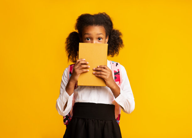 害羞的非洲裔美国女学生躲在书后面，工作室拍摄图片下载