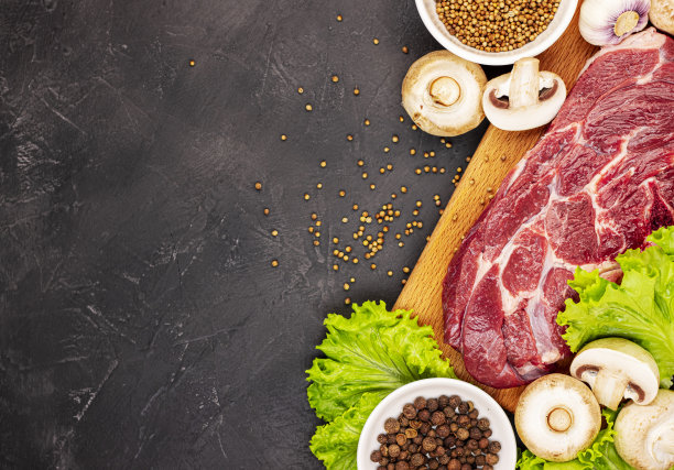 生的新鲜大理石肉牛排和调味料在黑色大理石背景，俯视图图片下载