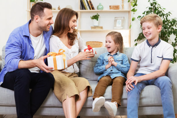 父母给坐在沙发上的孩子送礼物图片下载