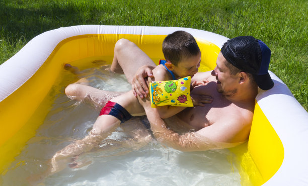 爸爸和他的儿子在游泳池里玩。孩子和父亲在室外游泳池玩得很开心，溅起水花，大笑。父亲节。图片下载