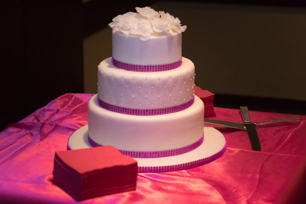 粉红色的桌子上放着黑色背景的白色婚礼蛋糕图片下载