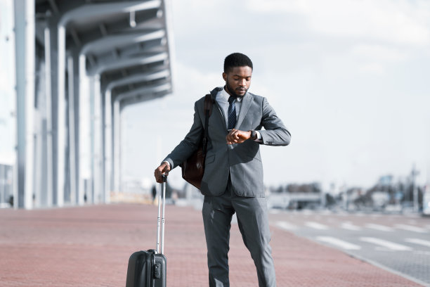 非洲商人拿着旅行箱在机场外看手表图片下载