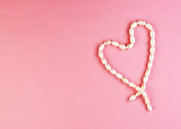 白色的心形珠子在美丽的粉红色背景上。女性的珠宝图片下载