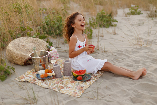 快乐可爱卷曲的小女孩拿着一块西瓜在夏季假期在海滩野餐。图片下载