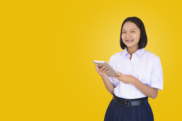 穿制服的亚洲学生使用黄色背景的笔记本电脑。图片下载