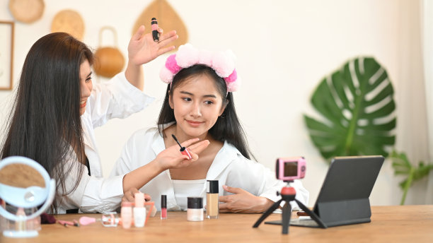 女性们正在木制梳妆台上通过网络视频展示如何化妆。图片下载