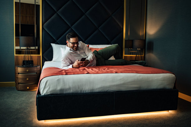 一个轻松优雅的男人躺在床上用智能手机聊天的肖像。图片下载