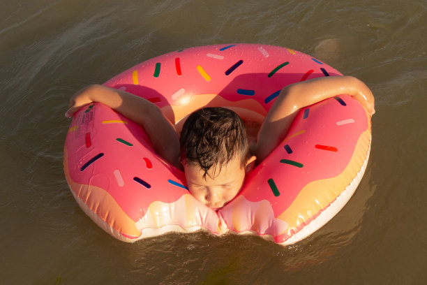 一个快乐的5岁男孩在阳光明媚的日子里，骑着一个甜甜圈形状的充气圈在海里游泳。图片下载
