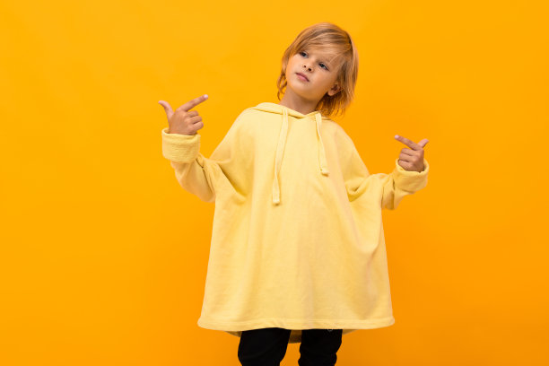 酷酷的金发男孩，巴拿马巴拿马穿着一件浅色帽衫，戴着眼镜在黄色演播室背景摆姿势图片下载