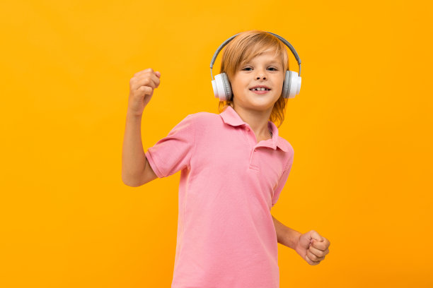 一个穿着粉色t恤的欧洲金发男孩戴着白色耳机在黄色背景上听音乐图片下载