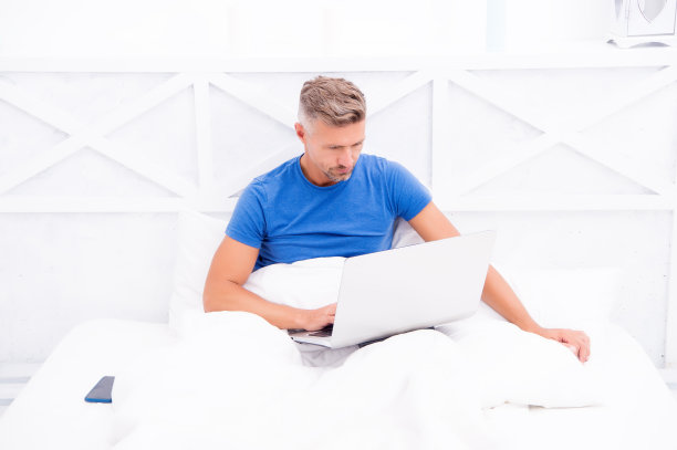 居家办公检查消息。睡在床上的成熟男人。商人与计算机。潮人在笔记本电脑上工作。卧室变成了新的办公室。远程工作。网上购物。在线交流图片下载