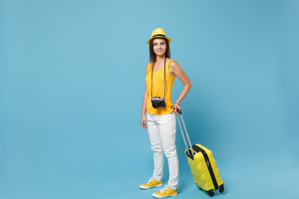 旅行者女游客黄色休闲服，帽子与手提箱照片相机孤立在蓝色背景。女乘客周末外出旅游度假。航空飞行旅程概念图片下载