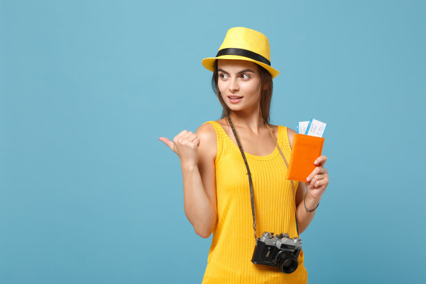 旅行者女游客在黄色的夏季休闲服帽子持票相机孤立在蓝色的背景。女乘客周末外出旅游度假。航空飞行旅程概念。图片下载