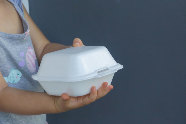 孩子的手拿着外卖泡沫饭盒。一次性食物容器，靠近。图片下载