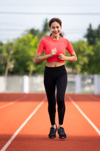 年轻的健身女性跑步者在早上在城市的体育场跑道上慢跑锻炼。2019冠状病毒病大流行期间，女运动员在城市体育场锻炼身体。健康和娱乐库存照片。图片下载