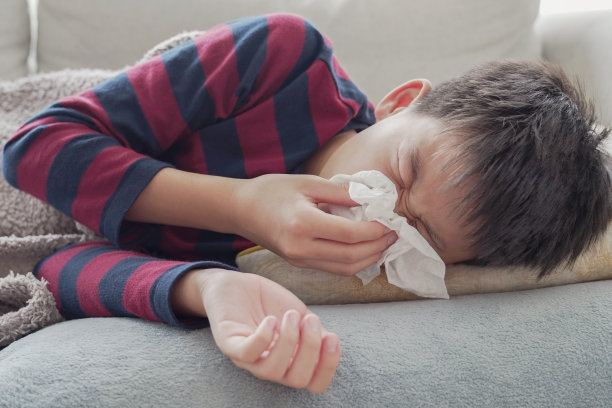 混合亚洲生病的十几岁的男孩打喷嚏和躺在家里的沙发上，保健概念图片下载