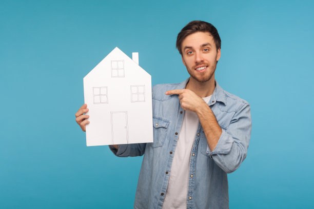 肖像欢快英俊的工人牛仔衬衫指着纸房子和微笑满意图片下载