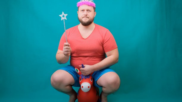 一名身穿粉色t恤、头戴耳坠、蓄着胡须的英俊古怪男子手持魔杖骑着独角兽。一个有趣的巫师笑话，用来实现一个愿望图片下载