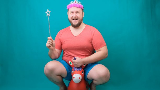 一名身穿粉色t恤、头戴冠冕、蓄着胡须的英俊男子骑在独角兽上，手里拿着一根魔杖。一个有趣的巫师笑话，用来实现一个愿望图片下载