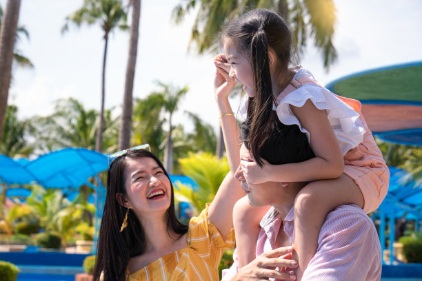 爸爸、妈妈和女儿在游乐园玩。主题公园里的家庭。图片下载