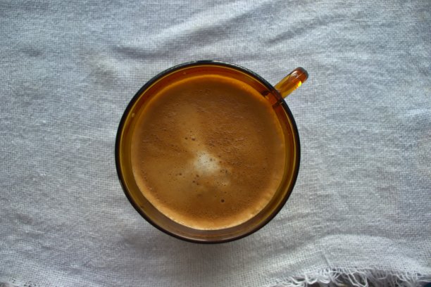 一杯带有泡沫的卡布奇诺或拿铁的俯视图，盛在一个琥珀玻璃杯子里，放在一条粗糙的白色边缘毛巾上。图片下载