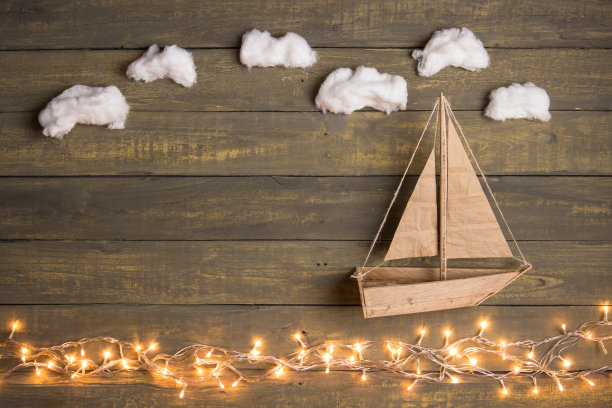 旅行和冒险的创意概念-玩具船在木制的背景与棉花云。圣诞彩灯如海浪图片下载