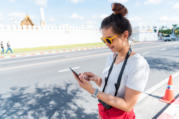 一位女游客站在街头微笑着用手机叫出租车。图片下载