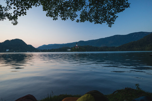斯洛文尼亚的清晨湖水流血。平静的湖面，山后初升的太阳，阿尔卑斯山。前景中的睡袋，特里格拉夫国家公园的户外探险。图片下载
