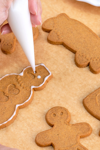 年轻女子是装饰圣诞节姜饼屋饼干饼干在家里的糖霜包，关闭，生活方式。图片下载