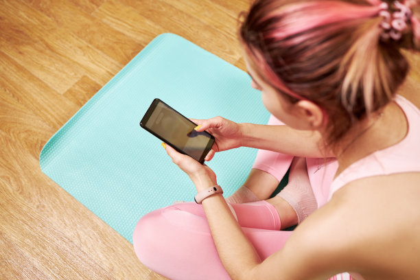 白人女性，粉红色头发和粉红色运动布，使用智能手机设备。关闭了。女孩触摸装置屏幕。在线健身概念。图片下载