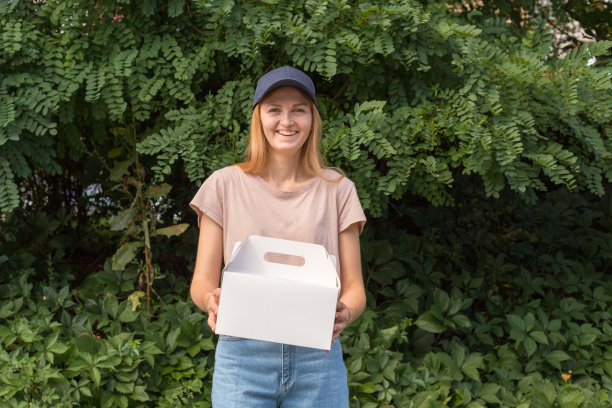 女快递员，蓝帽，甜点，无标记纸盒。送货服务的概念。广告区域。图片下载