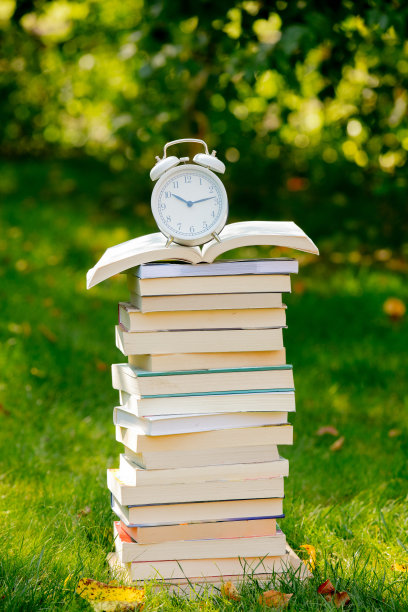 秋天的绿草地上有一堆书和一个闹钟图片下载