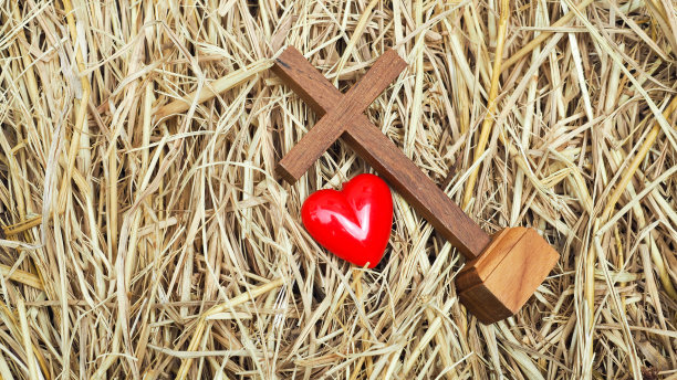木制的圣十字和干稻草上的红心。概念:耶稣生在马槽里，充满爱心。圣诞节和基督诞生，说明对基督的爱。图片下载